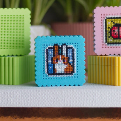 Small embroidery boxes in green, blue, pink, and yellow with perforated lids showing cross stitch bunny and ladybug examples