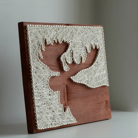 String art moose silhouette made with ivory thread and nails on a stained wooden base, finished DIY string art kit for adults displayed at an angle.