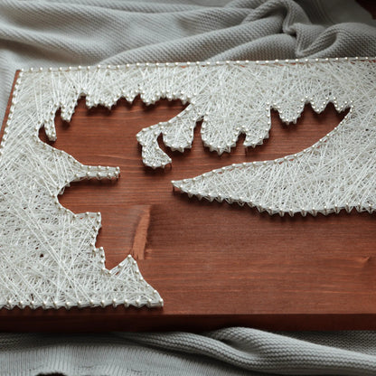 Close-up of a moose silhouette string art piece showing ivory thread wrapped around nails on a stained wooden base, highlighting the texture and stringing detail of a DIY string art kit for adults.