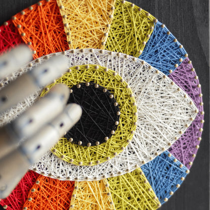 Close-up of a Third Eye string art sign showcasing intricate rainbow-colored threading and a black pupil centerpiece.