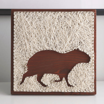 Artistic depiction of a capybara silhouette on string art with a wooden frame.