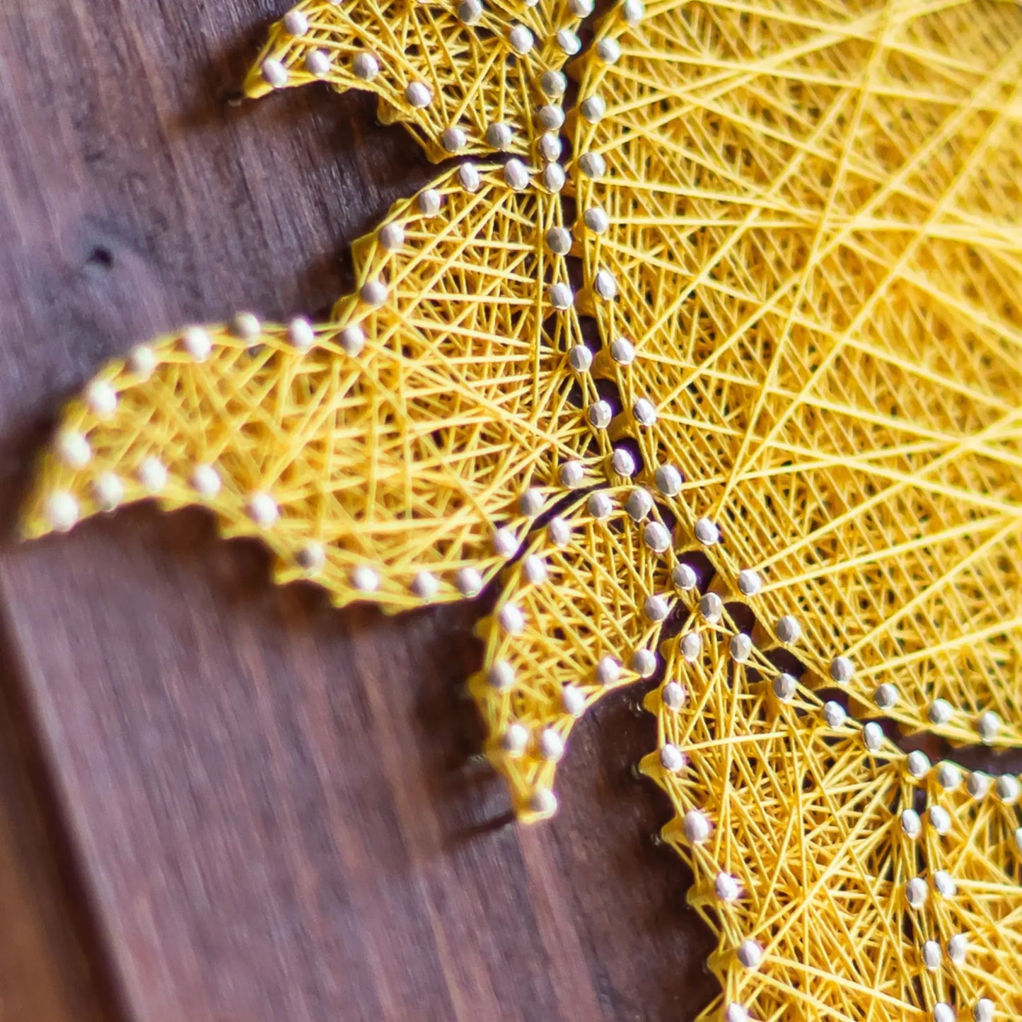 Detailed view of a vibrant yellow sun string art design on a wooden background, perfect for adding a touch of sunshine to any space. Available as a digital pattern.