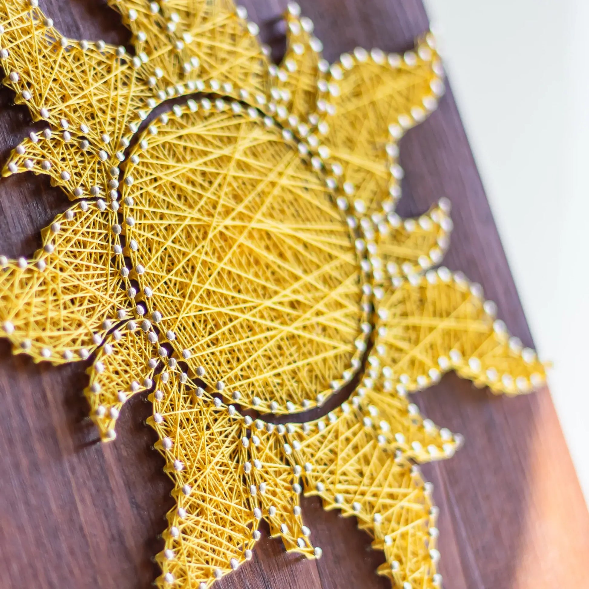 Side view of a vibrant yellow sun string art design on a wooden background, perfect for adding a touch of sunshine to any space. Available as a digital pattern.