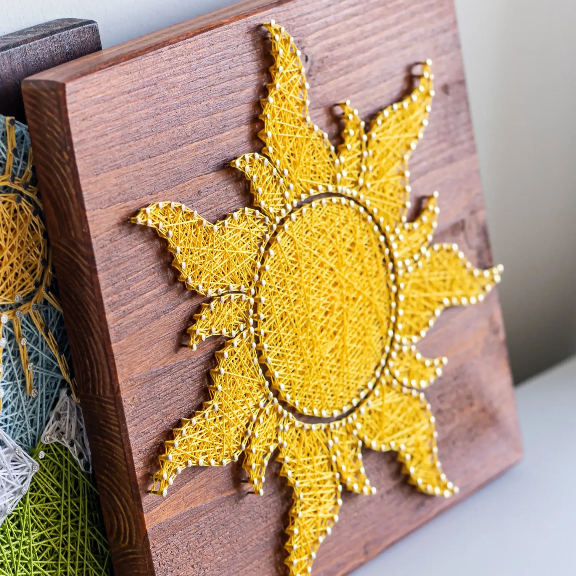 Side view of a vibrant yellow sun string art design on a wooden background, perfect for adding a touch of sunshine to any space. Available as a digital pattern.