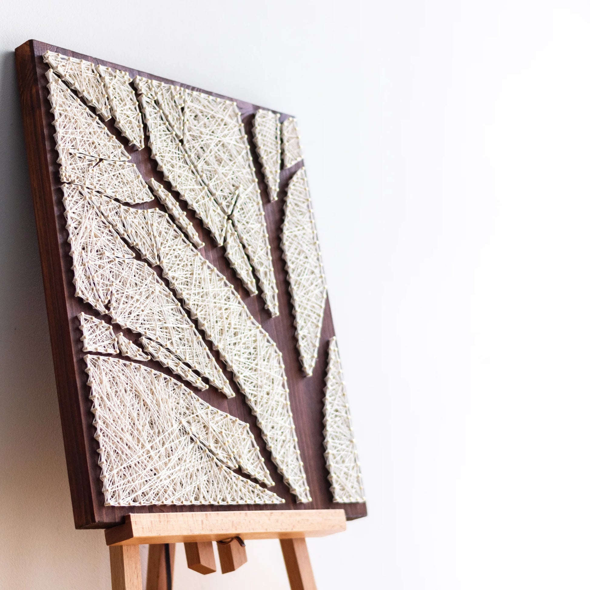 Side view of a completed tree silhouette string art made with ivory threads, showcasing the textured layering on a dark wooden panel.