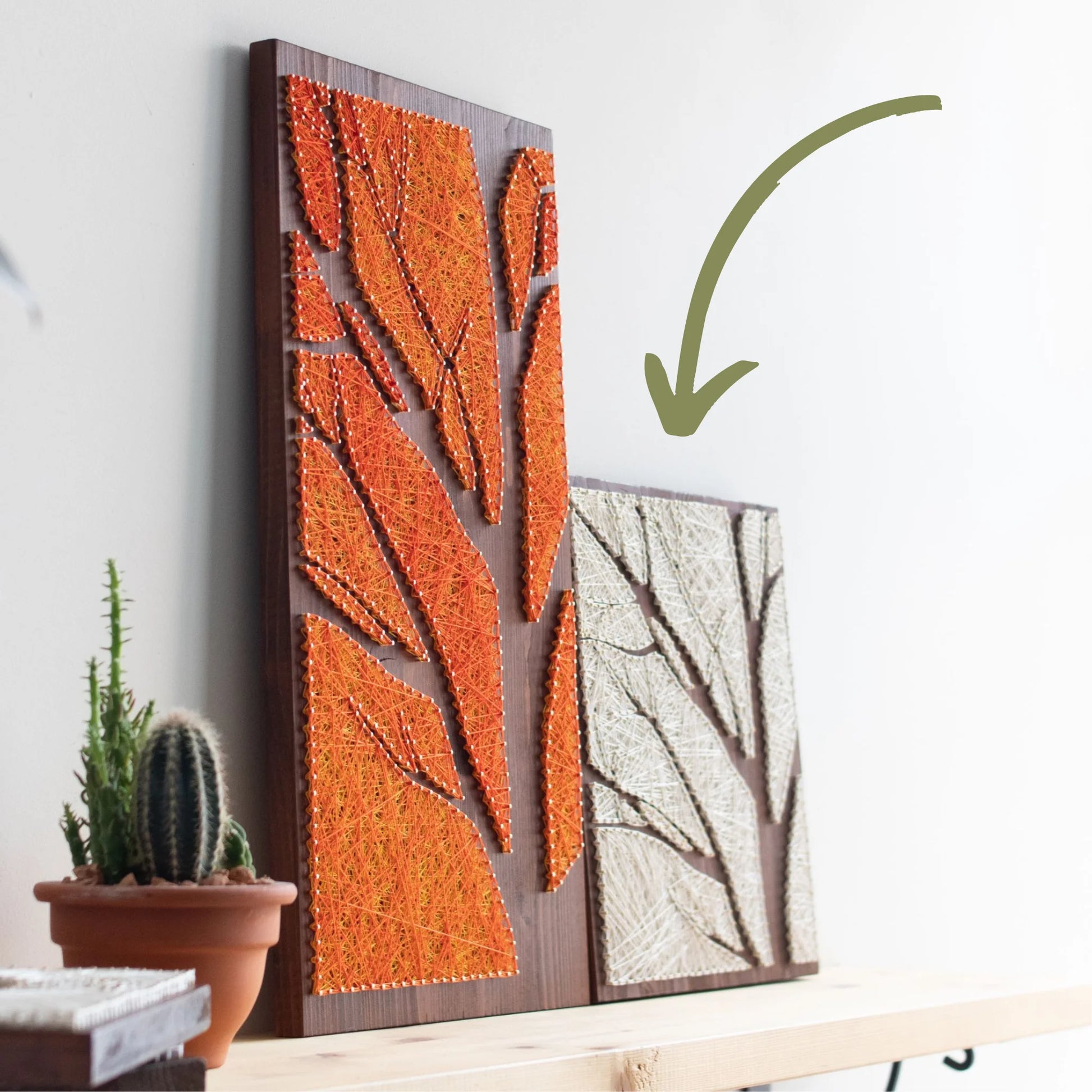 Two finished tree silhouette string art pieces, one with orange threads and the other with ivory, displayed on a wooden shelf, made by using string art pattern from GoodStrings