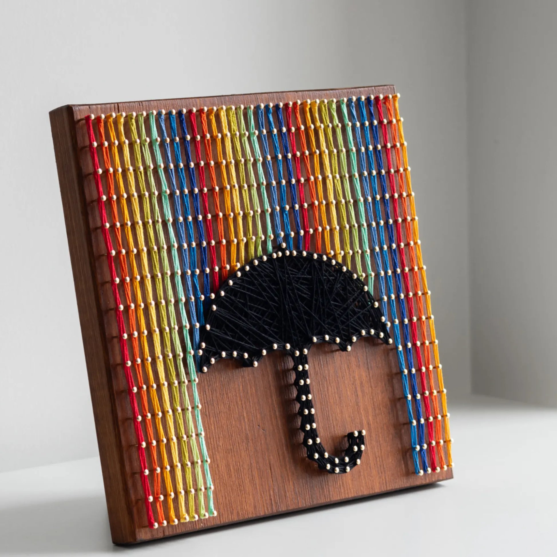 Umbrella and rainbow string art piece displayed on a white shelf.