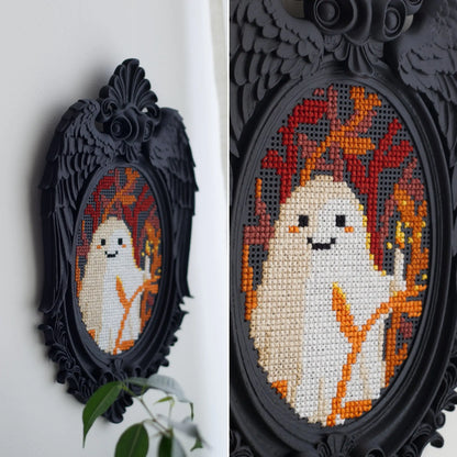 Black Victorian angel wing cross stitch frame with ghost embroidery mounted on wall and close-up detail showing perforated stitching surface and baroque ornate border for gothic whimsigoth wall decor
