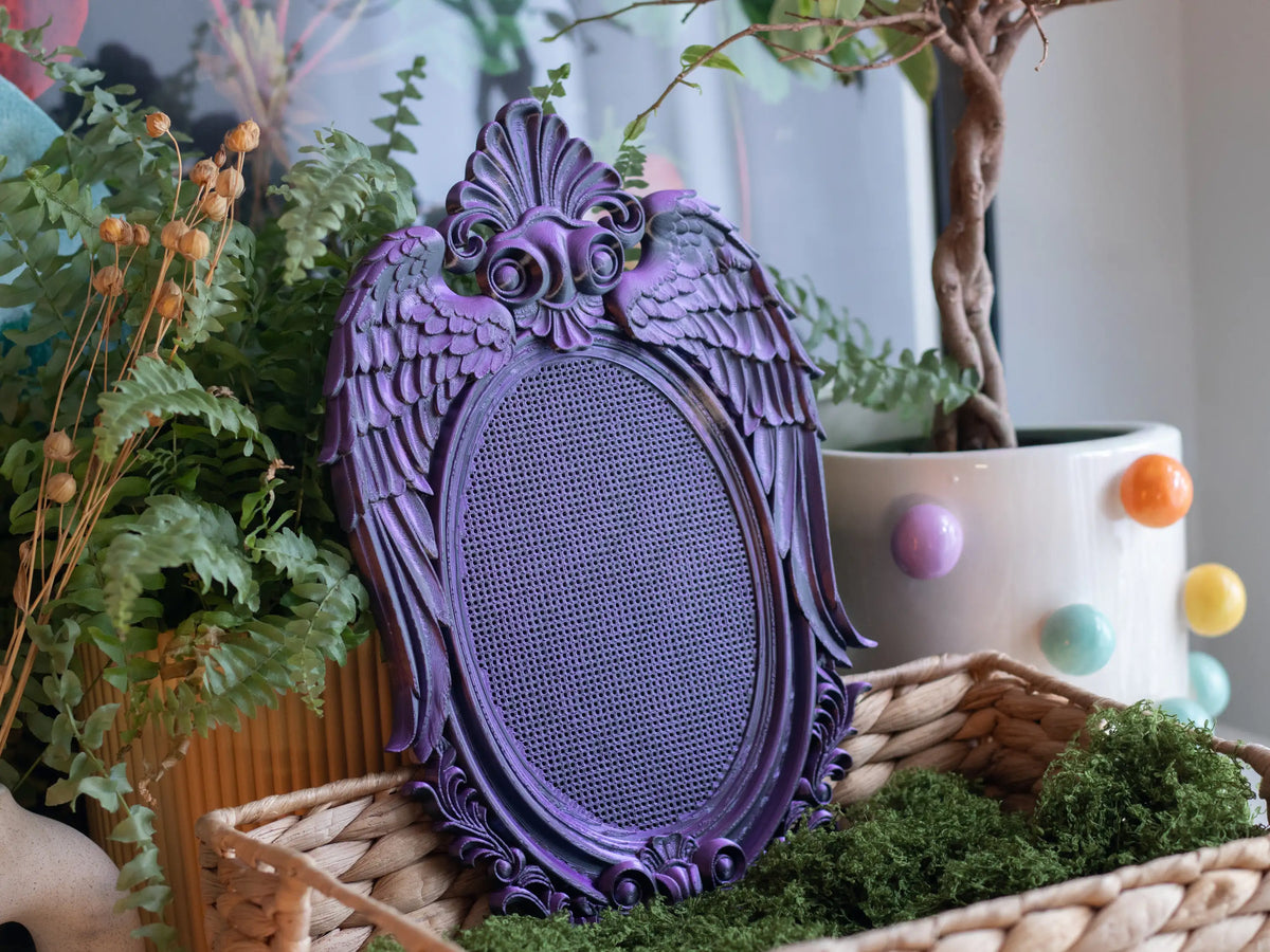 Purple 3D printed angel wing cross stitch frame in a wicker basket with moss and ferns, whimsigoth decor