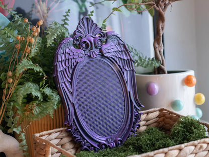 Purple 3D printed angel wing cross stitch frame in a wicker basket with moss and ferns, whimsigoth decor