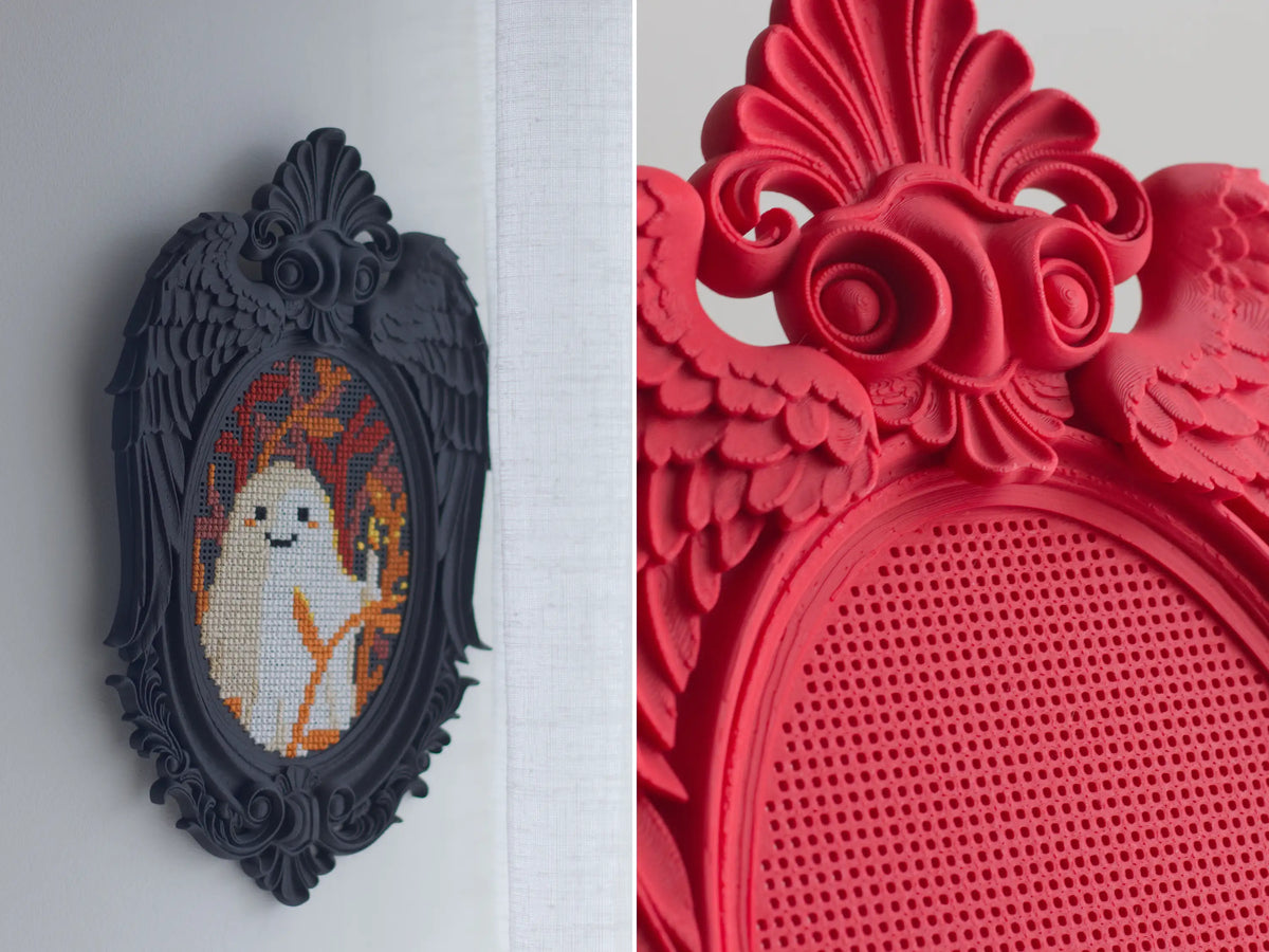 Black angel wing cross stitch frame hanging on a wall, and close-up of red frame showing rose and wing details