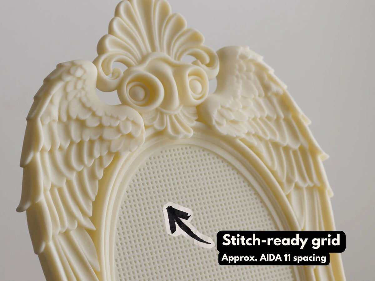 Close-up of cream 3D printed angel wing frame with baroque shell crest and stitch-ready grid, approx. Aida 11 spacing
