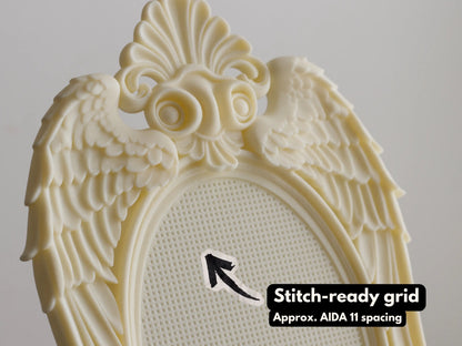 Close-up of cream 3D printed angel wing frame with baroque shell crest and stitch-ready grid, approx. Aida 11 spacing