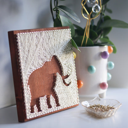 Decorative woolly mammoth string art styled with a colorful plant pot and a bowl of nails. Great for personalized craft decor.