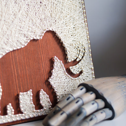Woolly mammoth string art pattern with a wooden hand prop showcasing its handcrafted details. A charming addition to DIY projects.